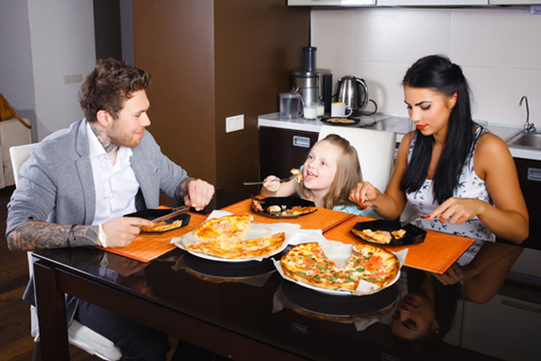 Parents and little girl sitting looking at each other enjoying pizza