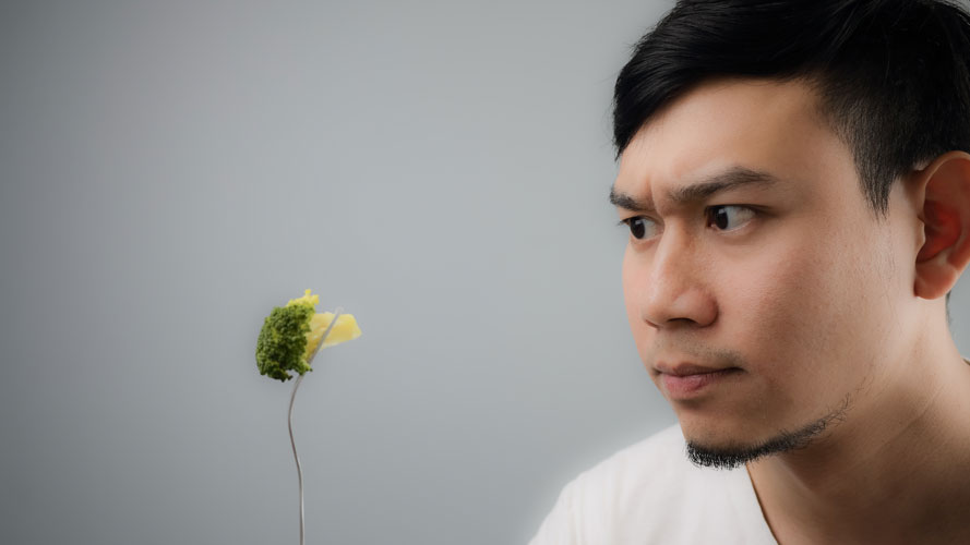 Young man looking skeptically at broccoli Young man looking skeptically at broccoli