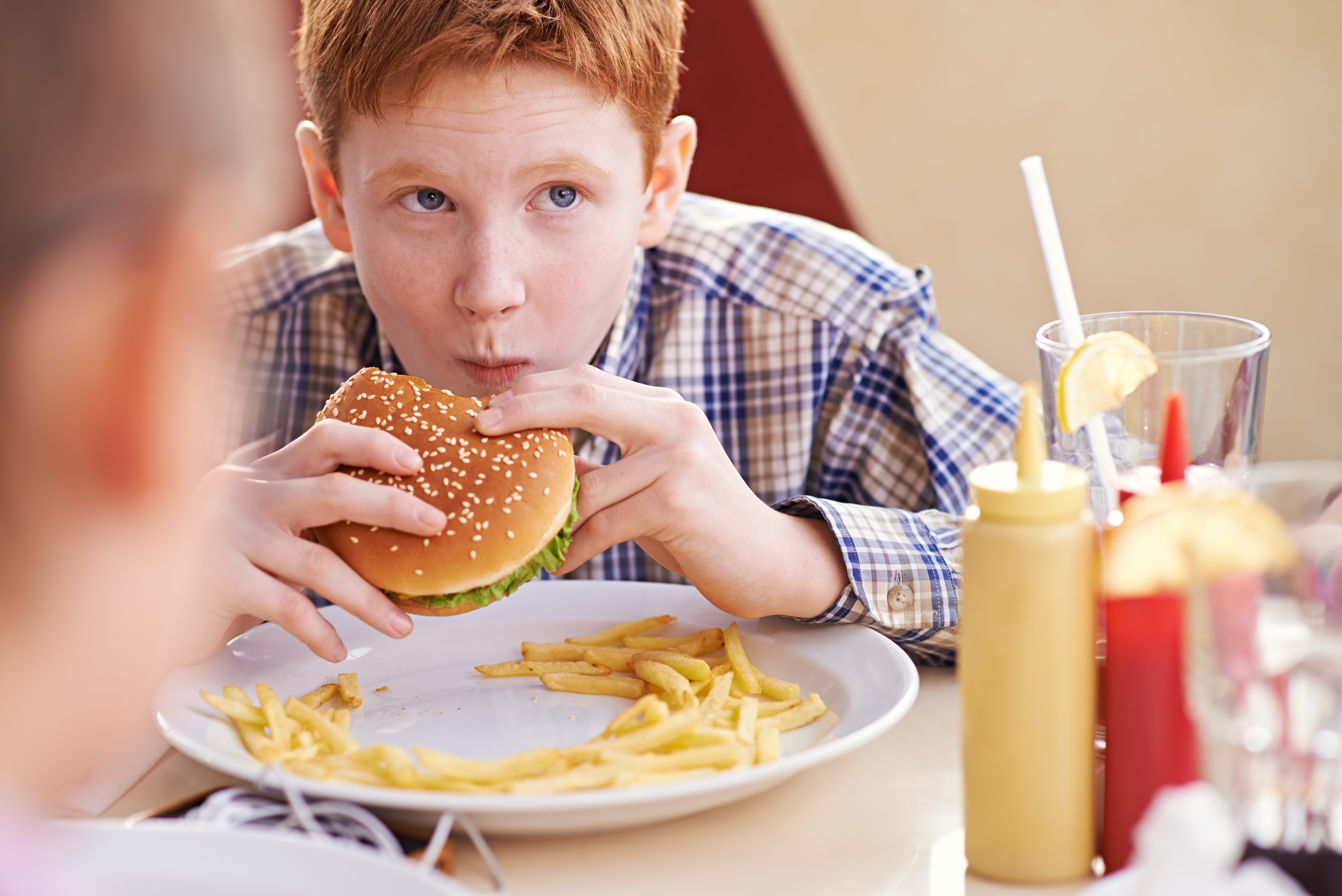 Teenage boy comfortably eating hamburger and fries