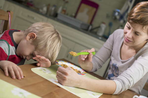 Mother trying to feed, boy has head down and hand up 