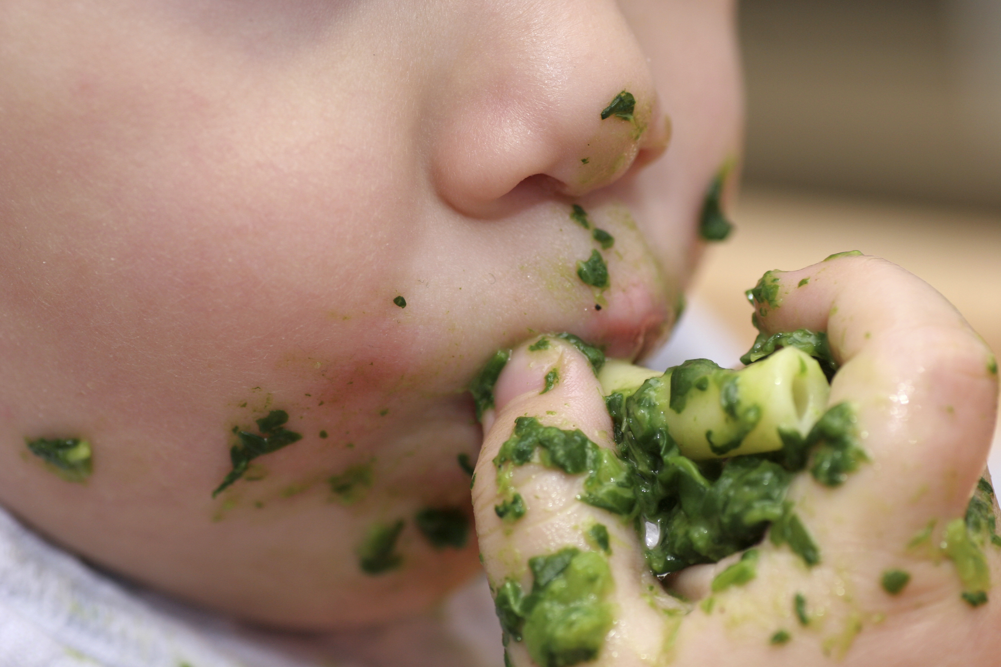 Closeup of messy hands and mouth of older baby eating pasta