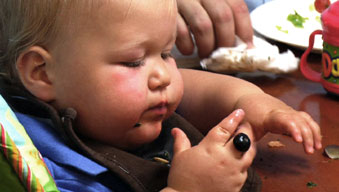 Chubby almost toddler struggling to feed himself at family meal
