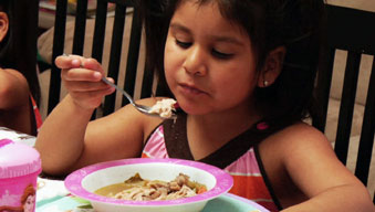 Preschooler sitting up nicely regarding food as she prepares to eat Preschooler sitting up nicely regarding food as she prepares to eat